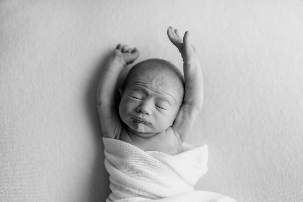 A newborn stretches out its arms in relaxation at their newborn photography session